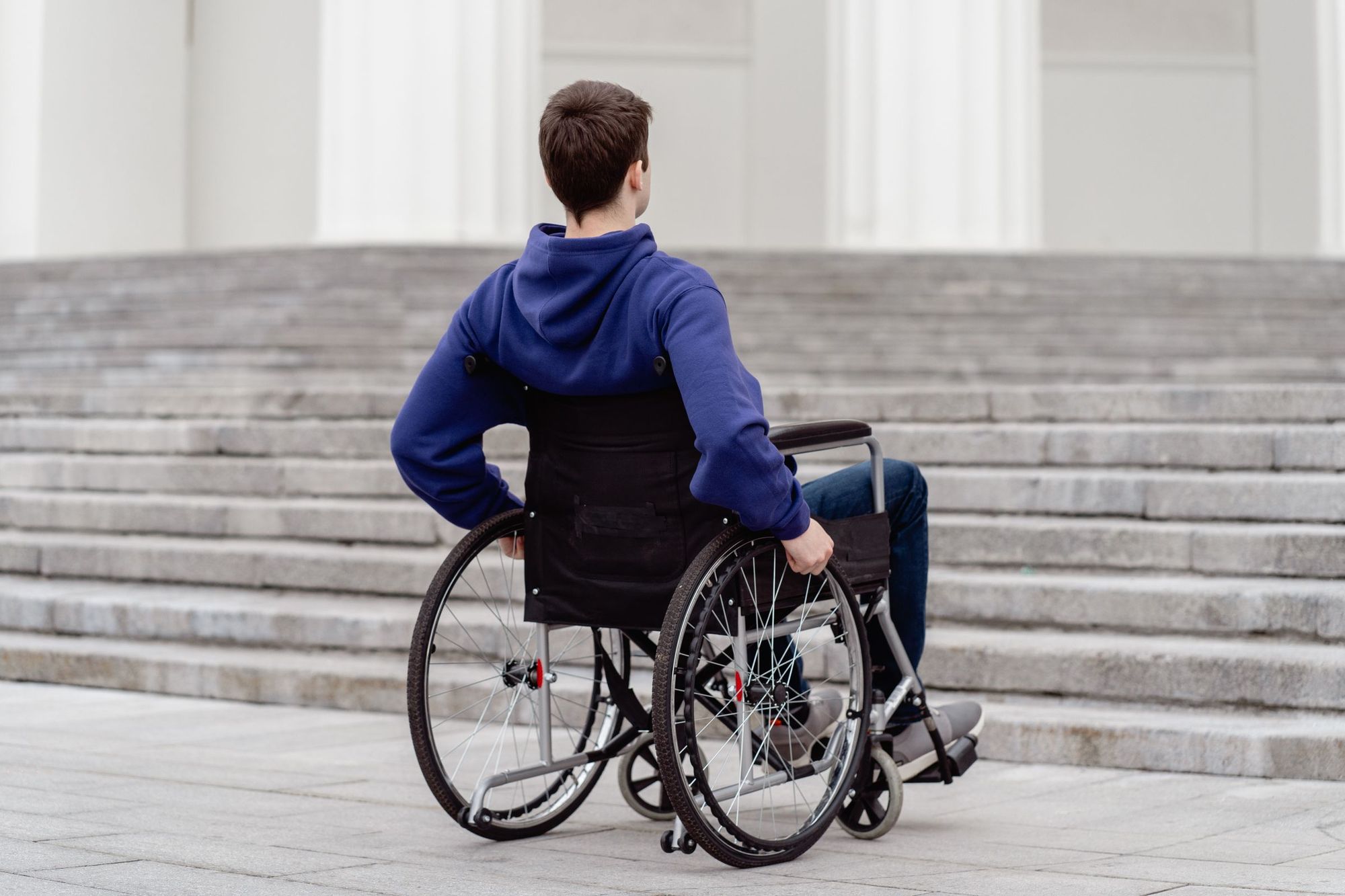 Un jeune homme en fauteuil roulant devant un grand escalier